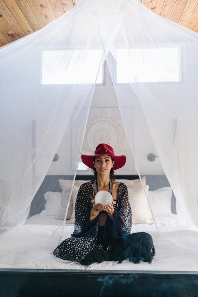 Woman in a peaceful indoor setting meditating with crystal ball, wearing a red hat and patterned dress.